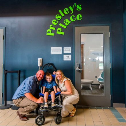 Jason Rudge, his wife, Sharon, and their son, Presley pose in front of the sensory room named for Presley at the Pittsburgh Airport.
